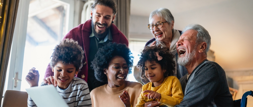 Multigenerational family laughing and gathered in front of laptop. 